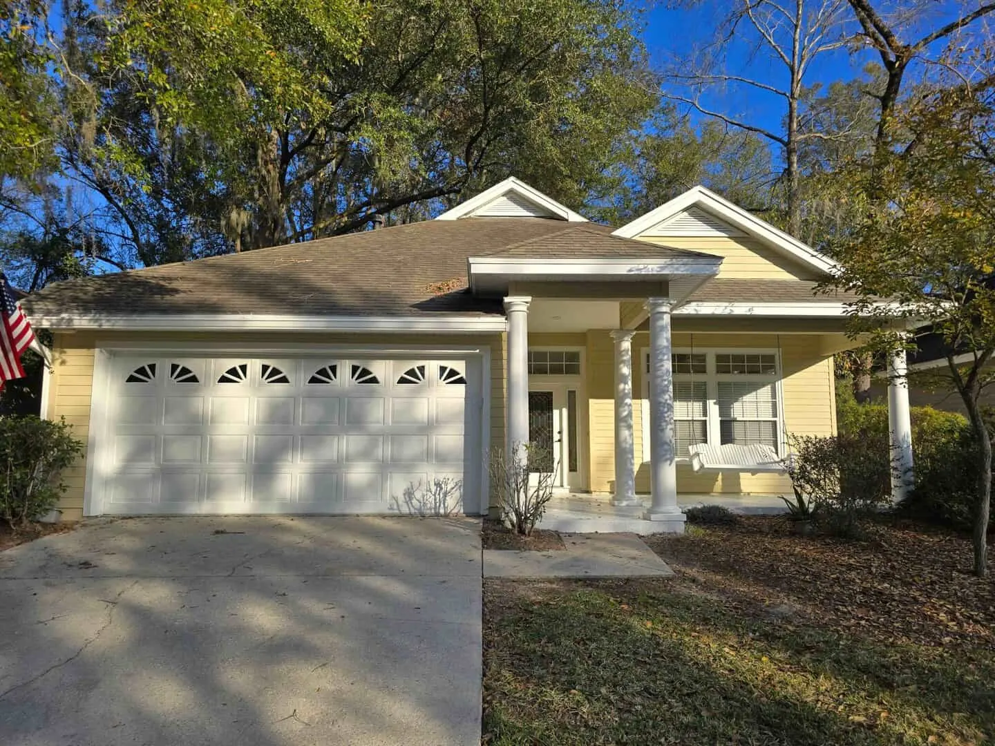 Pale yellow home with white columns, white trim and a white garage door